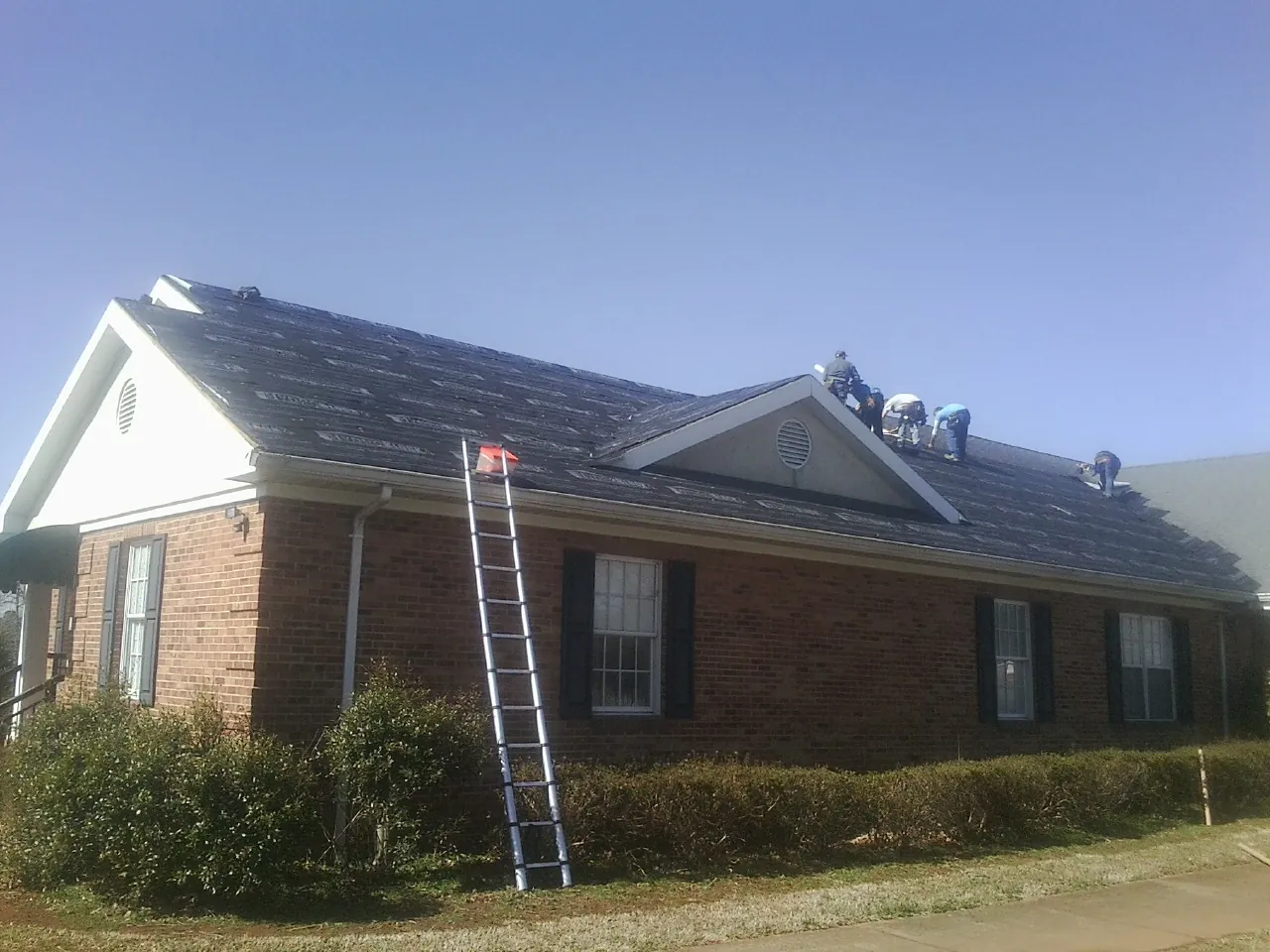 Crew tearing shingles off a brick ranch roof with a ladder set — Metal Roof Repair work by our crew in Waynetown
