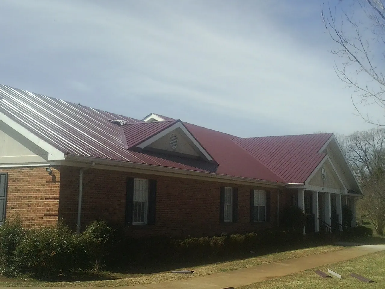 Red metal roof with gabled entries on a long brick building, from a Hail Damage Roof Repair job in Waynetown