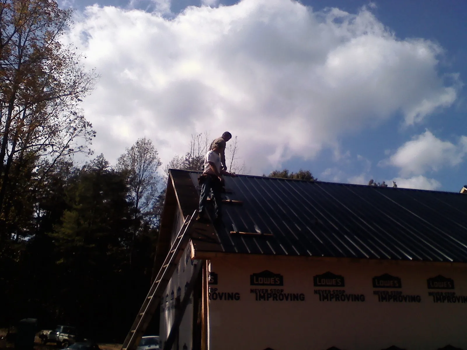 Roofer fastening dark metal panels high against a cloudy sky, from a Roof Inspection job in Waynetown
