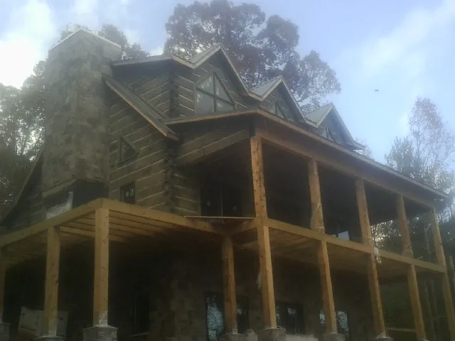 Stone chimney and dormers on a large log home with a timber porch in Waynetown