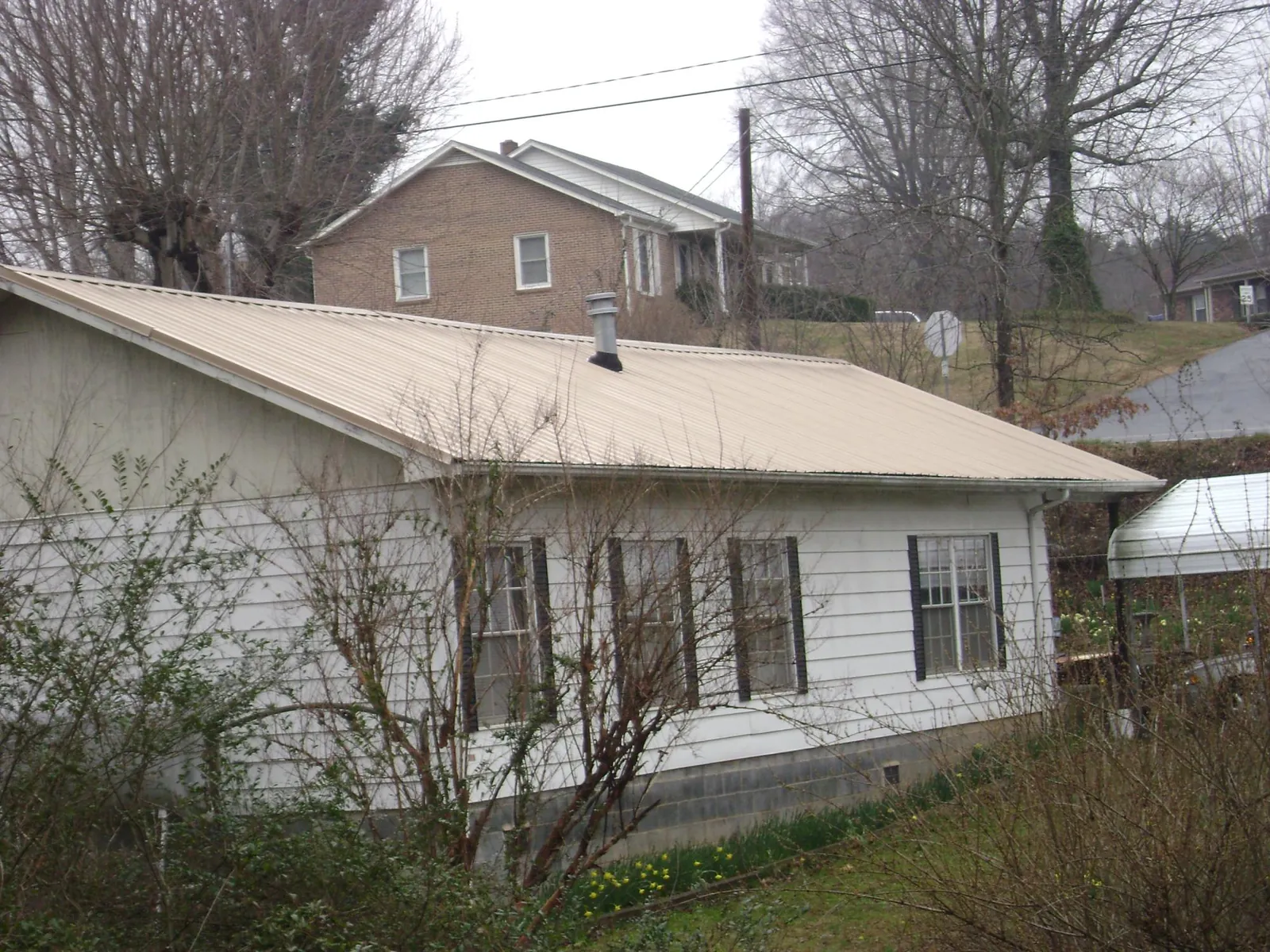 Tan metal roof on a white sided house set into a hillside — Commercial Roofing by Roofing Brothers in Waynetown